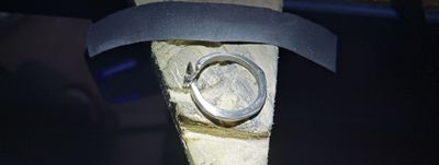 The ring wedged in a sanding jig, half polished bright and half still dull from coarse sandpaper